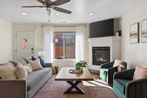 Ein Wohnzimmer mit Sofa, Sessel, Couchtisch, Kamin und Deckenventilator.