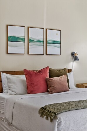 A bed with a white comforter, multiple pillows, and a throw blanket. There are three framed artworks above the bed. - Modern Rim Village Retreat- Pool, Hot Tub, Red Rock, and Mountain Views. (Moab)