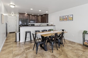 A modern kitchen with dark wooden cabinets, a stainless steel refrigerator, and a central island with stools. - Modern Rim Village Retreat- Pool, Hot Tub, Red Rock, and Mountain Views. (Moab)