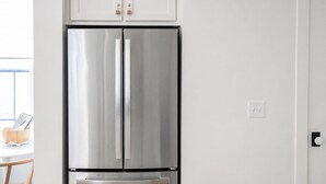 Ein Edelstahl-Kühlschrank mit separatem Gefrierfach, an einer weißen Wand montiert, darüber ein Holzschrank.