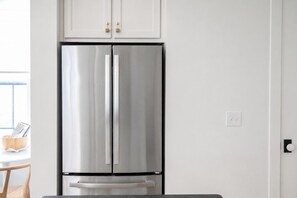 Ein Edelstahl-Kühlschrank mit separatem Gefrierfach, an einer weißen Wand montiert, darüber ein Holzschrank.