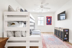 A bunk bed room with a ceiling fan, a TV, a patterned rug, and a cabinet with stickers. - The Lamar Landing, Pool+PB Court Velvet Ditch Villas (Oxford)