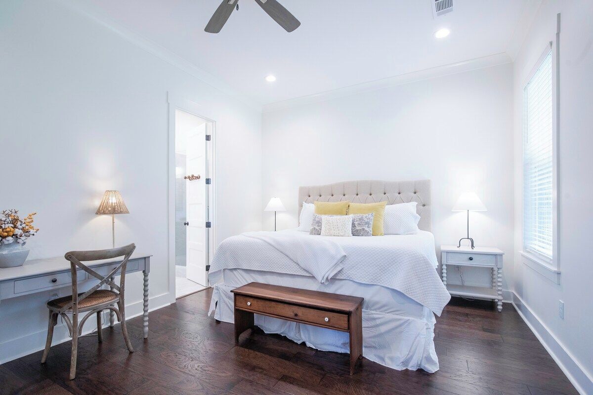 Um quarto com cama, mesas de cabeceira, uma cadeira e uma escrivaninha.