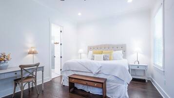 Um quarto com cama, mesas de cabeceira, uma cadeira e uma escrivaninha.