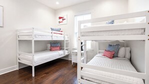 Une chambre avec deux lits superposés, un plancher en bois, un ventilateur de plafond et une fenêtre avec des stores.