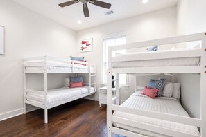 A room with two bunk beds, wooden flooring, a ceiling fan, and a window with blinds. - The Merion, 3BR+Game room by Velvet Ditch Villas (Oxford)