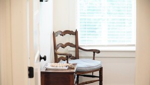 Une chaise en bois dotée d’un siège et d’un dossier rembourrés, placée près d’une fenêtre munie de stores.