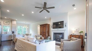 Un salon spacieux doté d’une cheminée, d’un ventilateur de plafond et d’un téléviseur fixé au mur au-dessus de la cheminée.