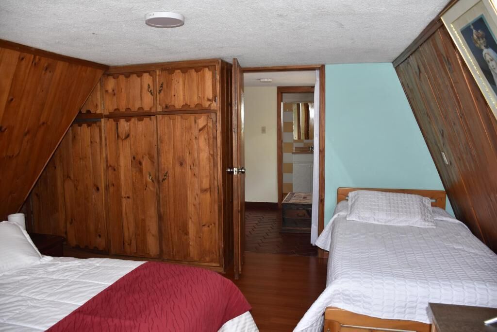 A bedroom with two beds, wooden wardrobe, and a door leading to a bathroom.