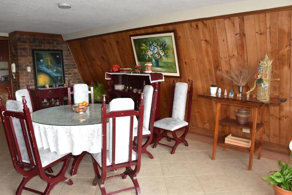 Uma sala de jantar com uma mesa redonda, cadeiras vermelhas, um aparador de madeira e um quadro na parede.