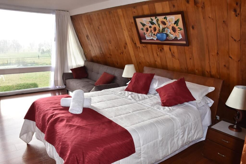 Une chambre d’hôtel avec un grand lit, une tête de lit en bois, un tableau représentant des tournesols et une vue sur l’extérieur.