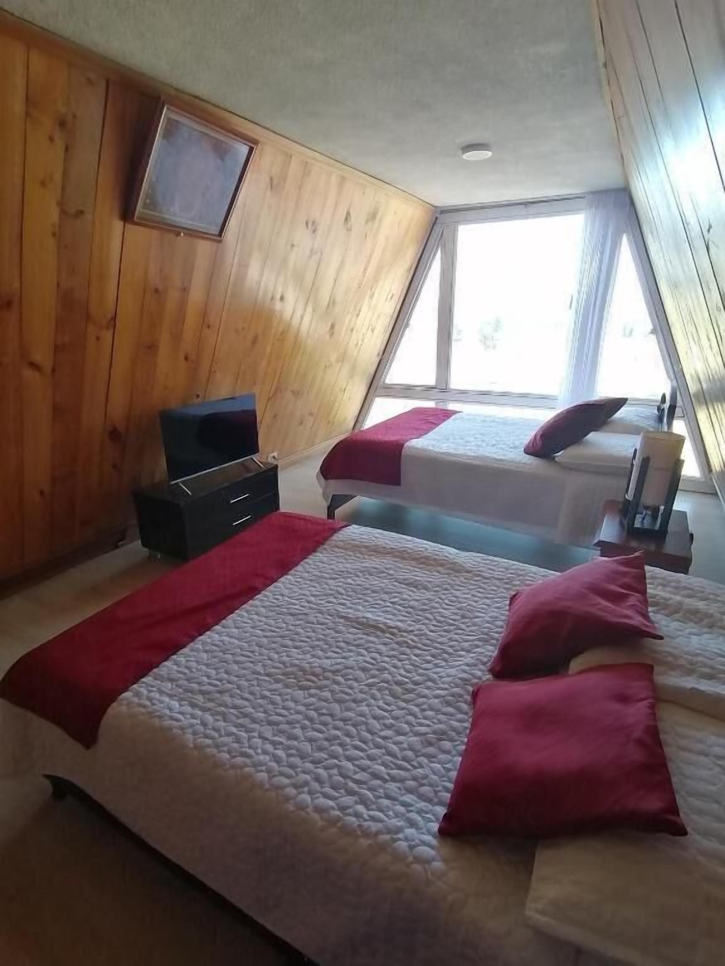 A bedroom with two beds, wooden walls, a TV, and a window.