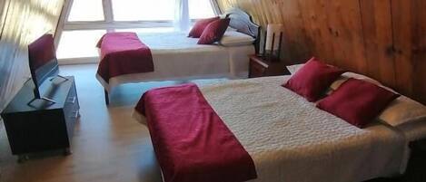 A room with two beds, wooden walls, a window, and a desk.