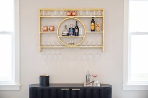 A wall-mounted shelf with various bottles and glasses, a round mirror, and a bar area with a black countertop. - The Social, 3mi to SQ + Pool by VelvetDitchVillas (Oxford)