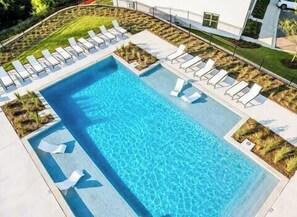 A rectangular swimming pool with a clear blue water surface, surrounded by a paved deck with white lounge chairs and small landscaped areas. - The Social, 3mi to SQ + Pool by VelvetDitchVillas (Oxford)