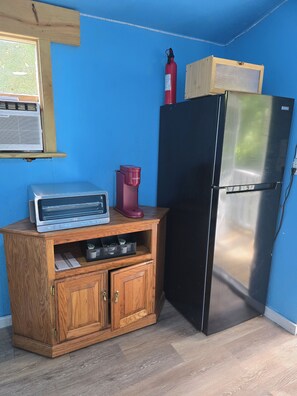 A compact kitchen with a black refrigerator, wooden cabinet, and a red kettle. - Cozy Cottage at Dancin' Dogs in Newberry FL. Dog friendly. (Newberry)