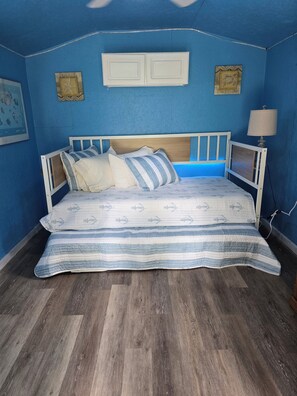 A bedroom with a bed, two bedside tables, a lamp, and a wall with a starfish decoration. - Cozy Cottage at Dancin' Dogs in Newberry FL. Dog friendly. (Newberry)