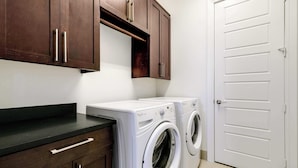 A laundry room with two white front-loading washing machines, wooden cabinets, and a white door. - Luxury 3BR Penthouse |Skyline Views |Uptown Dallas (Dallas)