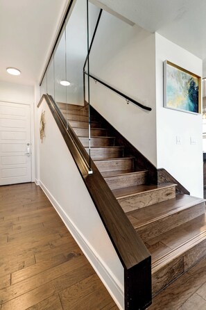 Una escalera de madera con barandillas de vidrio que conduce a un rellano con una puerta blanca.
