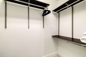 A closet with metal rods for hanging clothes, a black hanger, and a shelf with folded towels. - Luxury 3BR Penthouse |Skyline Views |Uptown Dallas (Dallas)
