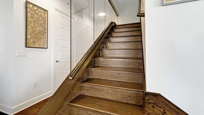A wooden staircase with a glass railing, white walls, and a framed artwork. - Luxury 3BR Penthouse |Skyline Views |Uptown Dallas (Dallas)