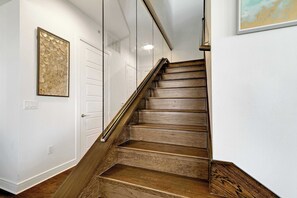 A wooden staircase with a glass railing, white walls, and a framed artwork. - Luxury 3BR Penthouse |Skyline Views |Uptown Dallas (Dallas)