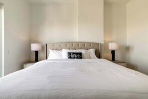 A neatly made bed with a tufted headboard, two bedside lamps, and a pillow with the word 'hope' on it. - Luxury 3BR Penthouse |Skyline Views |Uptown Dallas (Dallas)