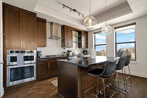A modern kitchen with stainless steel appliances, wooden cabinets, and a large island with bar stools. - Luxury 3BR Penthouse |Skyline Views |Uptown Dallas (Dallas)