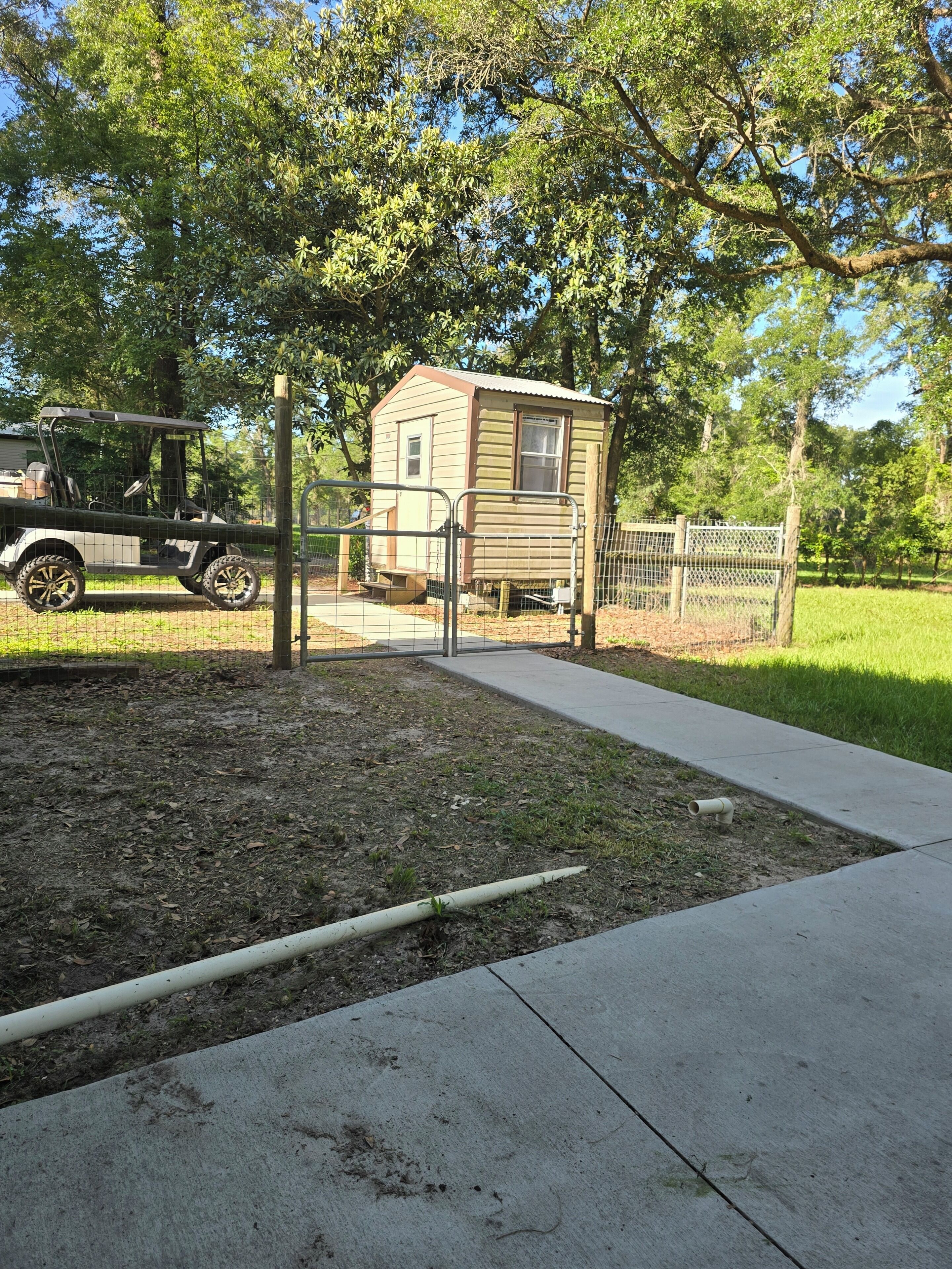A small wooden cabin with a metal gate, a concrete pathway, and a golf cart nearby.