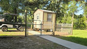 A small wooden cabin with a metal gate, a concrete pathway, and a golf cart nearby.