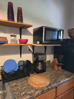A kitchen with a microwave, coffee maker, and wooden cutting board on the counter.