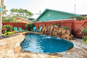 A swimming pool with a waterfall feature, surrounded by stone tiles and a red fence. - Heated Pool-Fun Game Room -Close to Beach-Pet Friendly (Galveston)