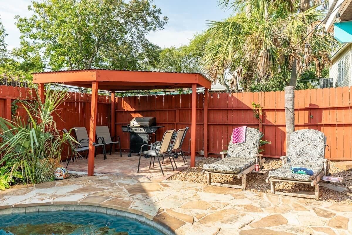 A backyard with a stone patio, a swimming pool, a barbecue grill, and outdoor furniture.