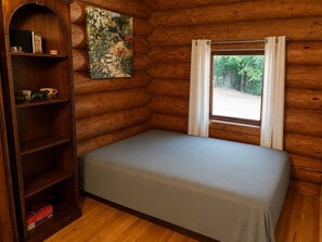 A log cabin room with a bed, a bookshelf, and a painting.