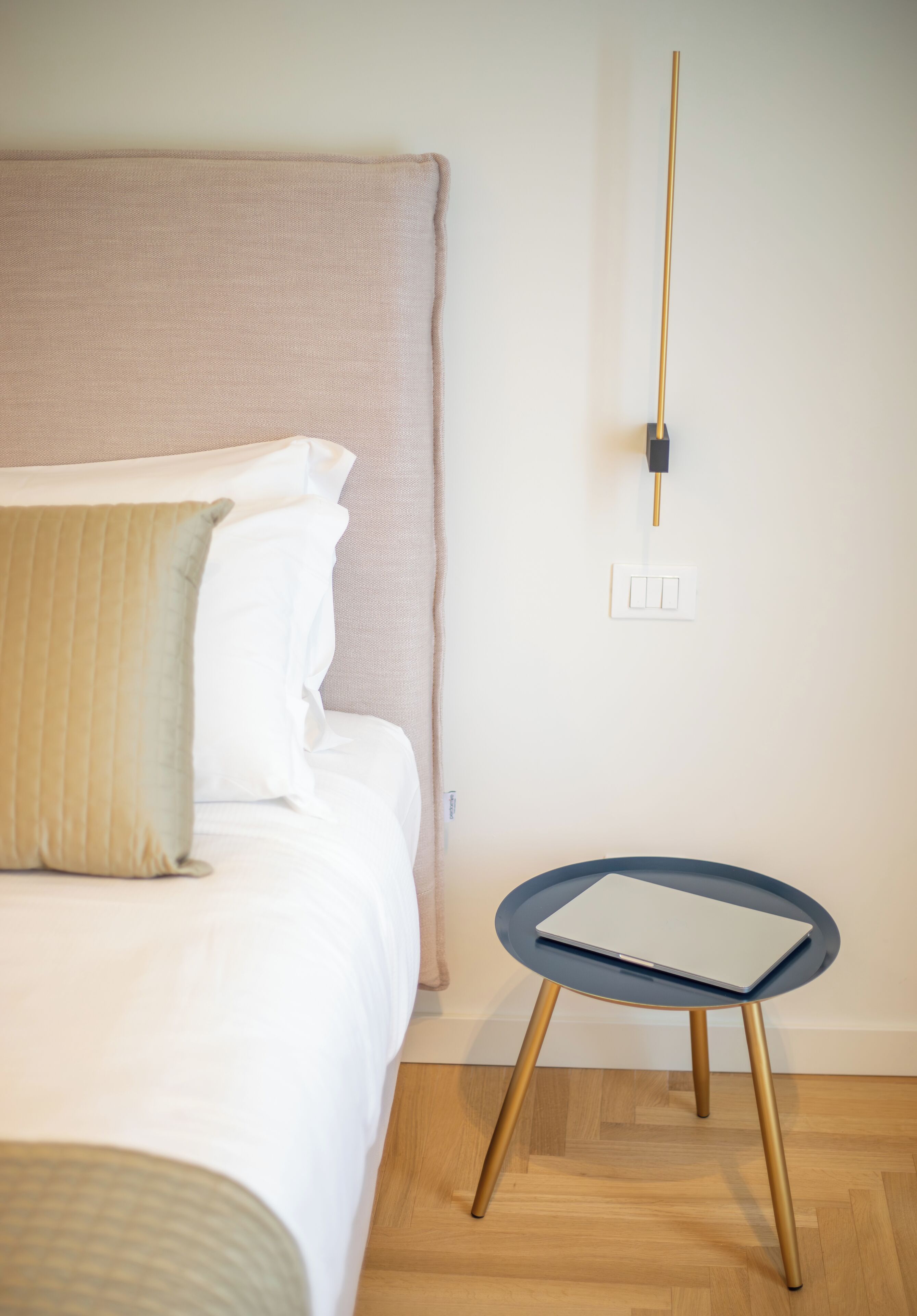Un lit avec une tête de lit, une table de chevet avec un ordinateur portable, et un luminaire fixé au mur.