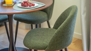 Una mesa de comedor con un plato de comida, un vaso de jugo de naranja y un tazón de limones. Hay dos sillas con tapicería verde.