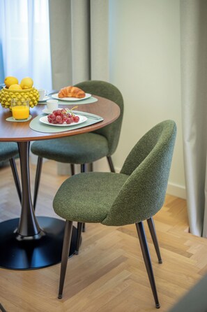 A dining table with a plate of food, a glass of orange juice, and a bowl of lemons. There are two chairs with green upholstery. - Luxury Boutique Apartment 4 in Palermo City Center, near the Central Station (Palermo)