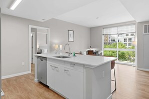 A modern kitchen with a central island, a built-in dishwasher, and a large window offering a view of the city. - Luxury Harborpoint Apt (Stamford, CT)