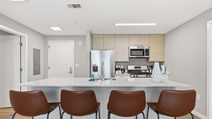 Una cocina moderna con una isla central, electrodomésticos de acero inoxidable y cuatro sillas marrones.