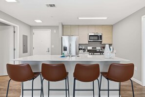 A modern kitchen with a central island, stainless steel appliances, and four brown chairs. - Luxury Harborpoint Apt (Stamford, CT)