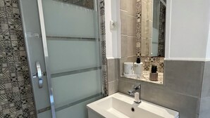 Ein Badezimmer mit Duschkabine aus Glas, einem weißen Waschbecken und einem Spiegel darüber sowie Wandfliesen mit Muster.