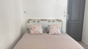 Ein Bett mit einer gesteppten Decke, zwei Kissen mit Blumenmustern, ein weißes Kopfteil und eine graue Tür.