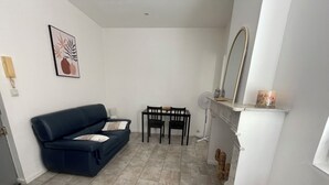 Ein Wohnzimmer mit einem dunkelblauen Sofa, einem kleinen Tisch mit zwei Stühlen, einem weißen Kamin und einem an der Wand befestigten Spiegel.