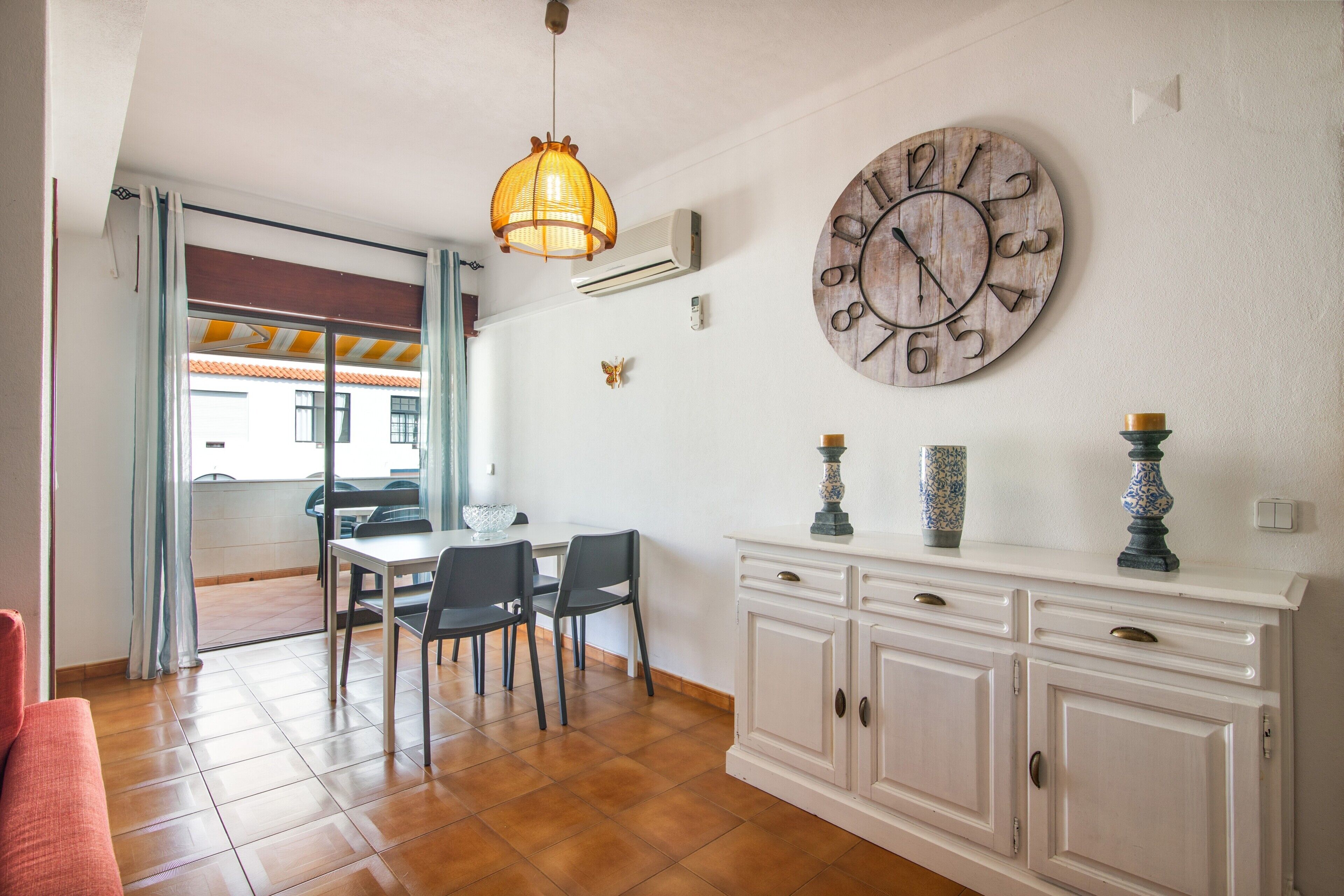 A dining area with a table and chairs, a decorative clock, and a cabinet with vases.