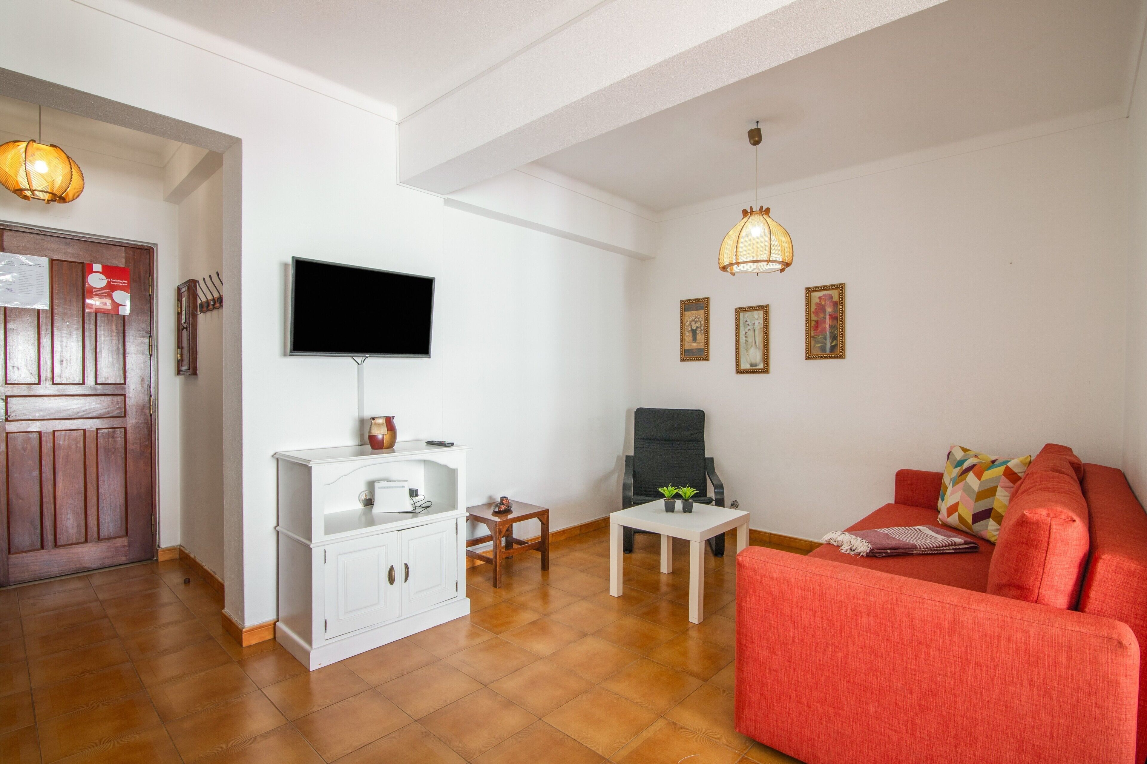 A living room with a television, a sofa, a coffee table, and a chair. There is a wooden door and a white cabinet.