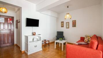 A living room with a television, a sofa, a coffee table, and a chair. There is a wooden door and a white cabinet.
