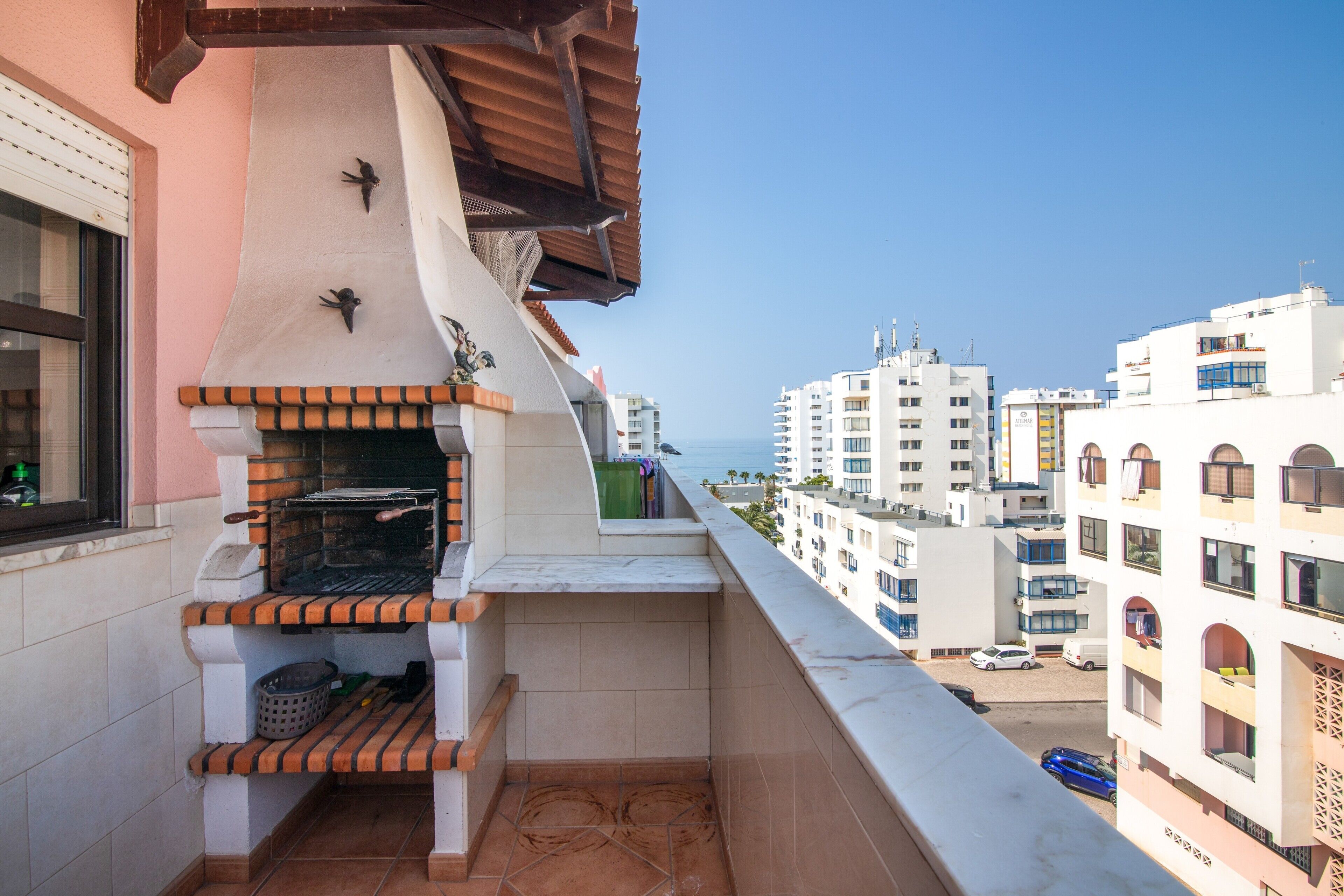 A balcony with a grill, a small statue, and a view of the sea and buildings.