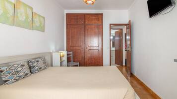 A bedroom with a bed, a nightstand, a lamp, a wardrobe, and a television mounted on the wall.