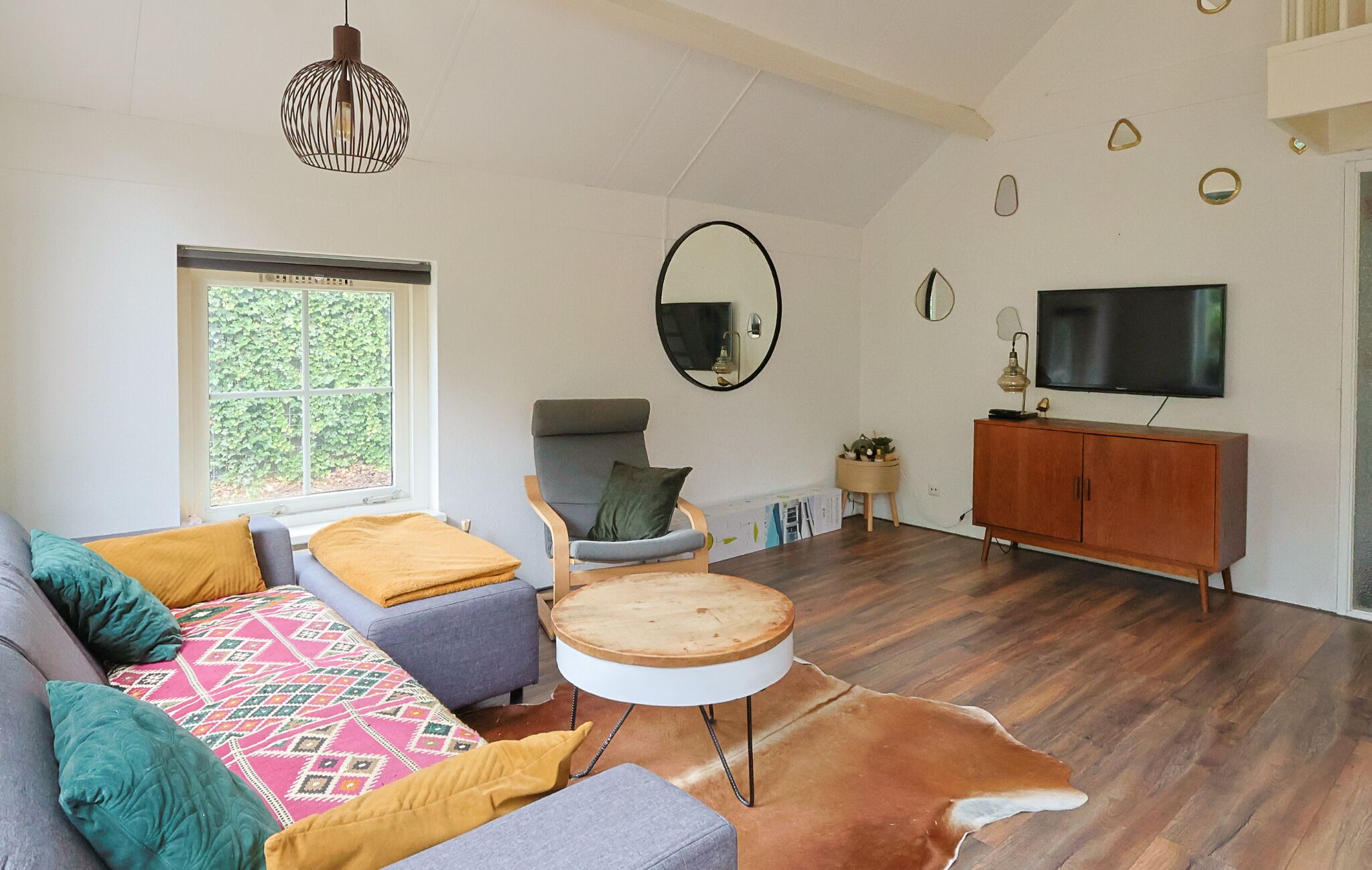 A living room with a sofa, armchair, round table, and a television.