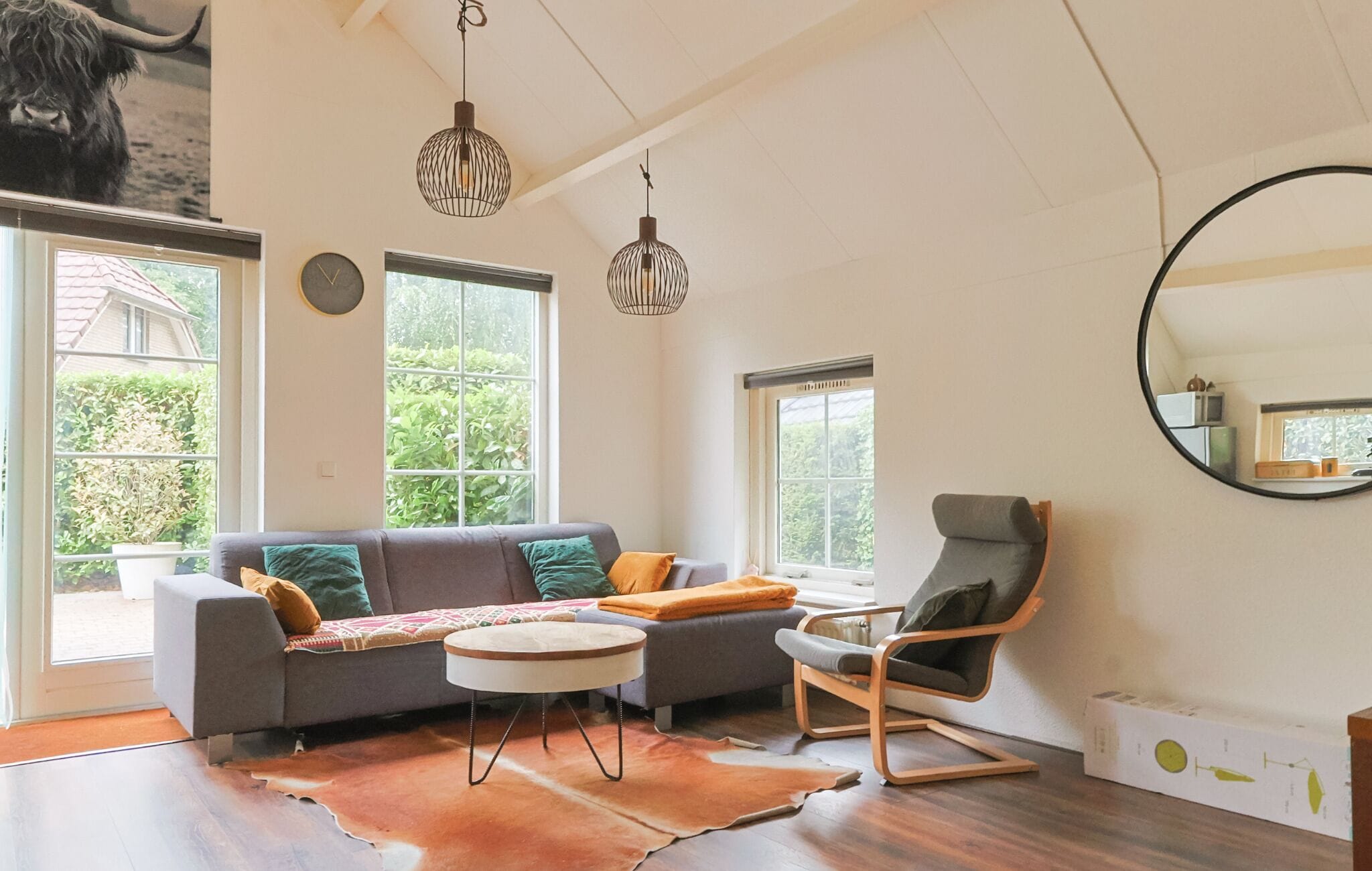 A living room with a sofa, a chair, a round table, and a large mirror.